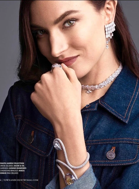 Close-up of a woman wearing a blue denim jacket and sparkling jewellery, including earrings, a necklace, a ring and a bracelet.