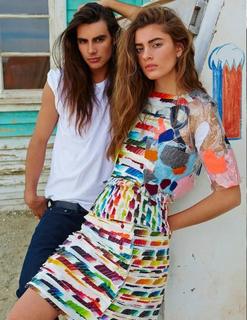 Fashion shot of a woman in a colorful short dress with a man wearing a white t-shirt and jeans near a weathered building.