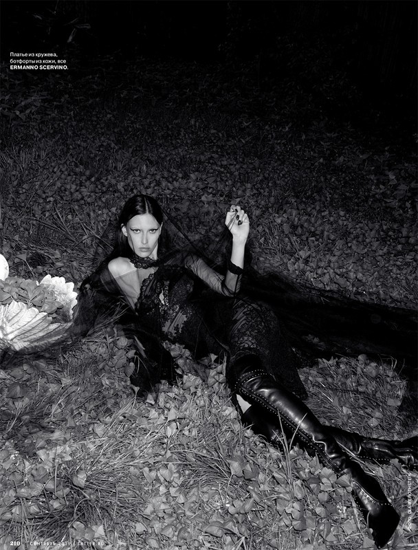 Model in black lace dress and leather boots lying on grass outdoors at night with make-up by Chris Colbeck