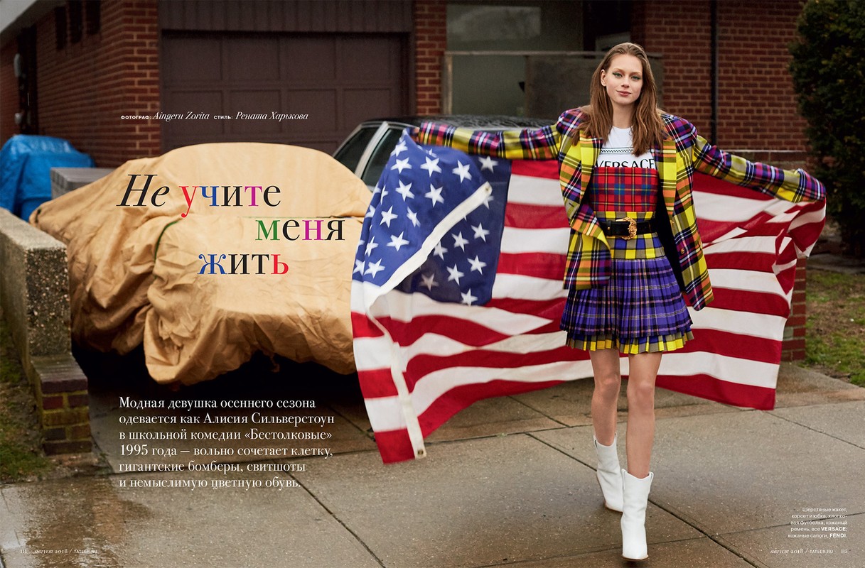 A fashionable woman strikes a pose outdoors with a vibrant American flag, wearing a yellow plaid blazer and a matching short skirt.