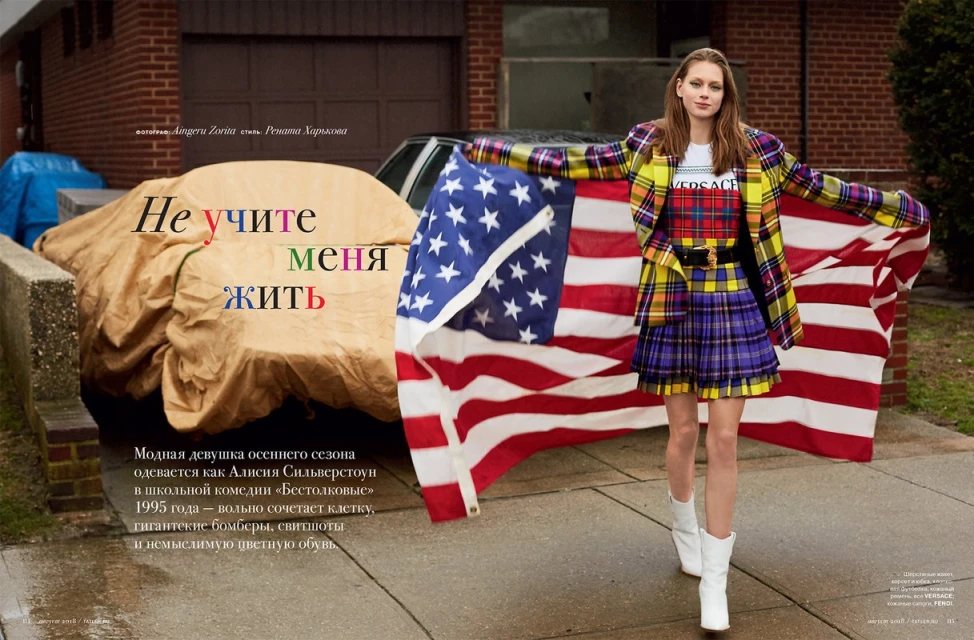 A fashionable woman strikes a pose outdoors with a vibrant American flag, wearing a yellow plaid blazer and a matching short skirt.