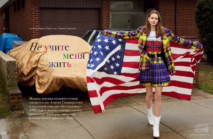 A fashionable woman strikes a pose outdoors with a vibrant American flag, wearing a yellow plaid blazer and a matching short skirt.