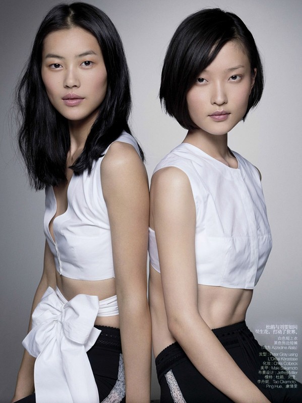 Two Asian women pose back-to-back in white crop tops and black bottoms against a gray background in a beauty and fashion editorial shot.