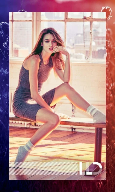 Indoor portrait of a young adult woman in a grey athletic dress, sitting on a bench in front of a window with natural light.