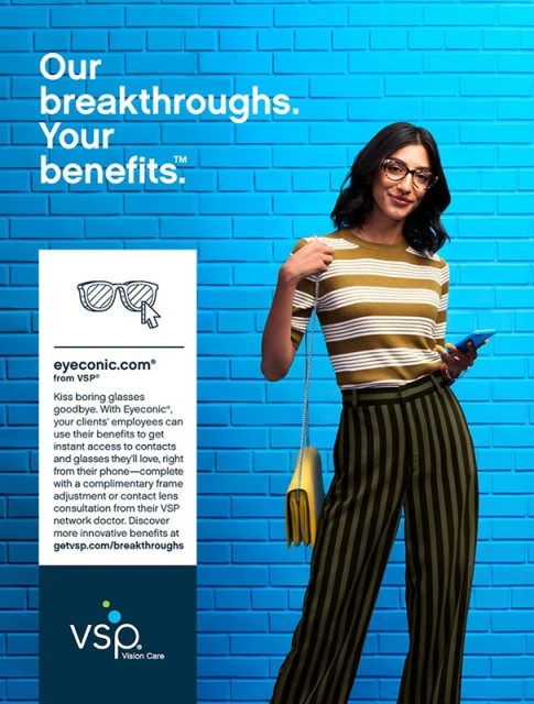 A woman wearing glasses holds a phone in front of a blue brick wall in an eye-catching ad for VSP Vision Care.