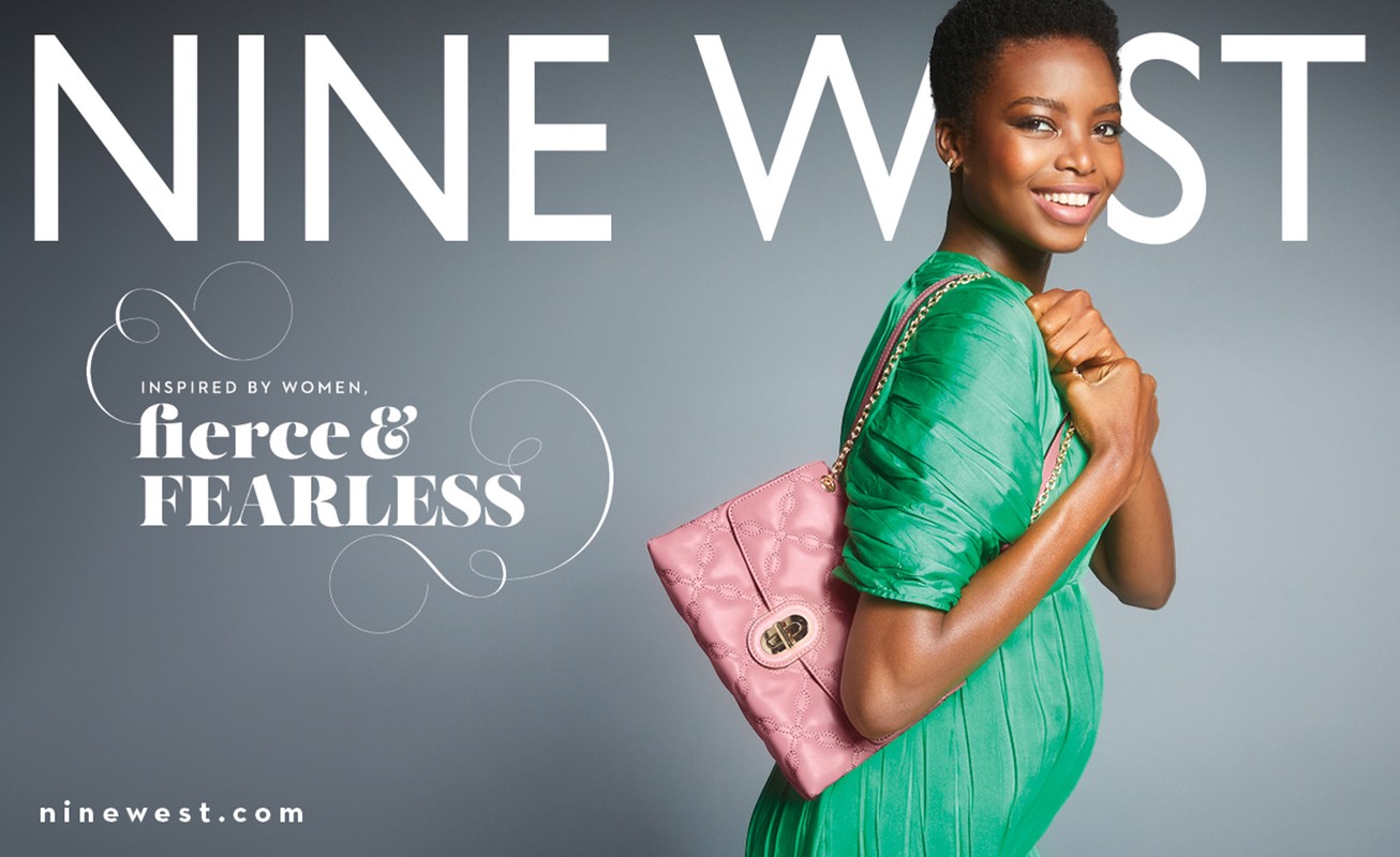 Nine West brand ad featuring a smiling African-American woman wearing a green dress, holding a pink quilted handbag, on a grey background.