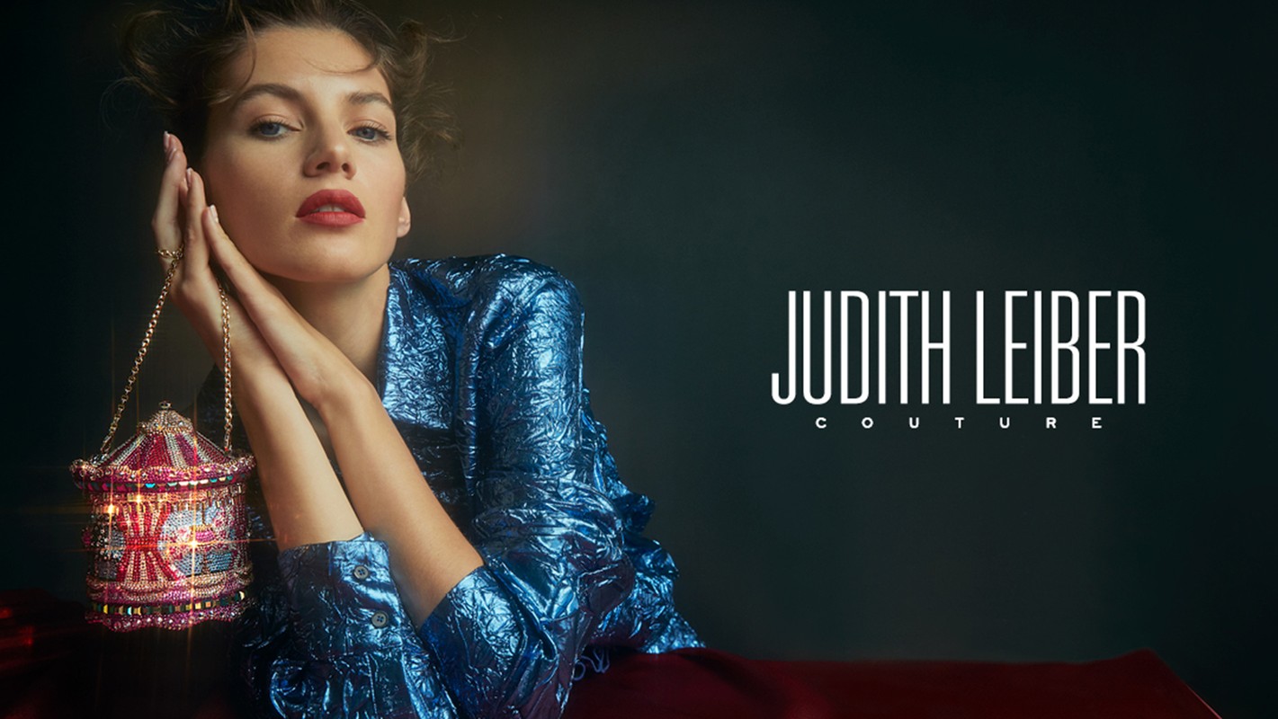 Fashion shot featuring a woman wearing a blue shimmering jacket, holding a decorative carousel-shaped clutch, against a dark backdrop.