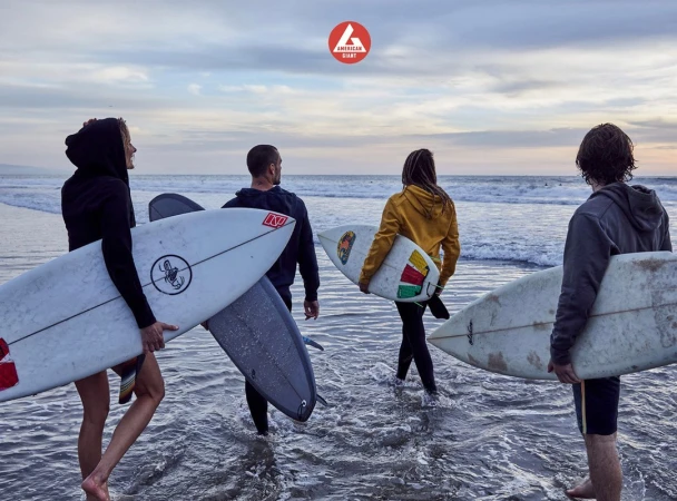 Group of four people walking into ocean with surfboards on a beach at sunset with an American Giant logo in the background.