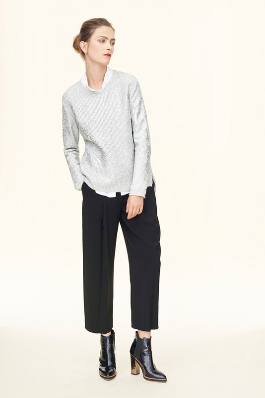 Model wearing a textured light grey sweater, white shirt, black trousers, and black heeled boots against white backdrop.