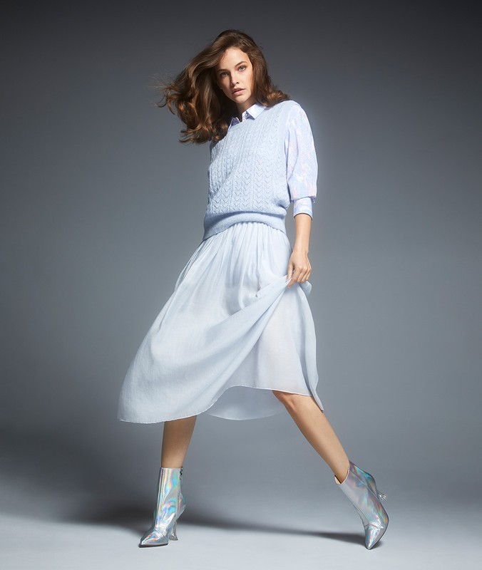 Full-length shot of a fashion model in studio wearing a light blue cable knit sweater, light blue chiffon skirt, and iridescent ankle boots.