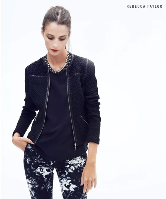 Fashion shot of a woman in a black textured jacket and floral pants. The woman is looking down, posing in front of a white background.