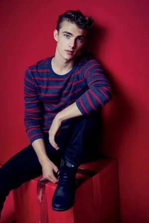 Young man in a striped blue and red sweater seated against a vibrant red studio background styled by Christine Baker