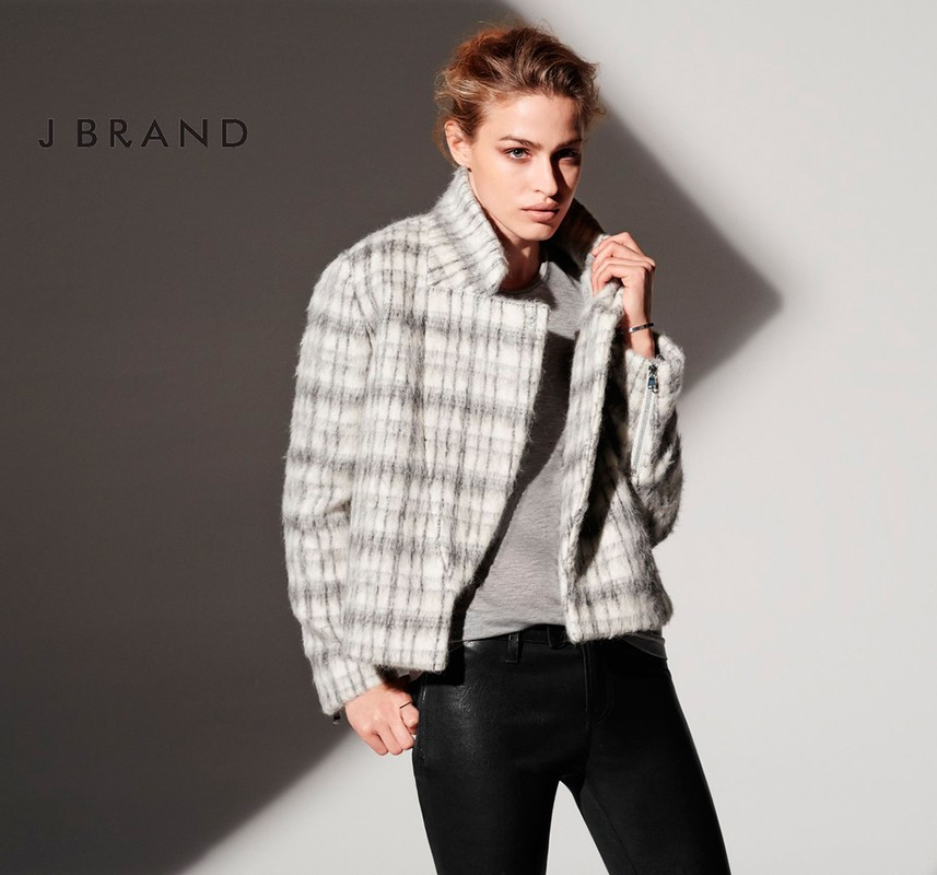 Model wearing a plaid jacket and black trousers against a neutral wall with wardrobe styling by Christine Baker.