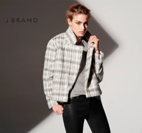 Model wearing a plaid jacket and black trousers against a neutral wall with wardrobe styling by Christine Baker.