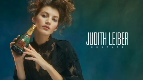 Woman in a black lace dress holding a crystal-embellished champagne bottle prop against a dark teal gradient background
