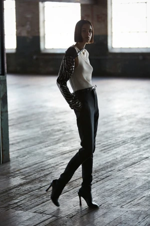 Model with short dark hair in sequin sleeve top and dark trousers in an industrial loft space.
