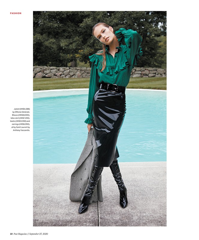 Fashion editorial shot of a model in a green ruffle top and black patent skirt and boots, standing near a pool outdoors.