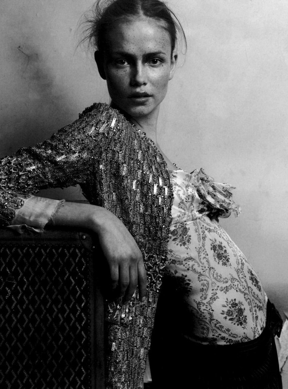 Monochrome portrait of a woman with an embellished jacket posing indoors near a dark cabinet, showcasing fashion and portrait photography.