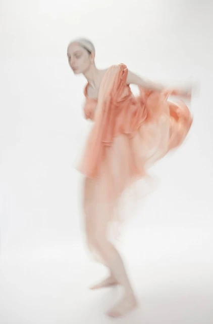 Abstract fashion photo featuring a blurred motion effect of a woman in a peach dress against a white background. Dreamy aesthetic.