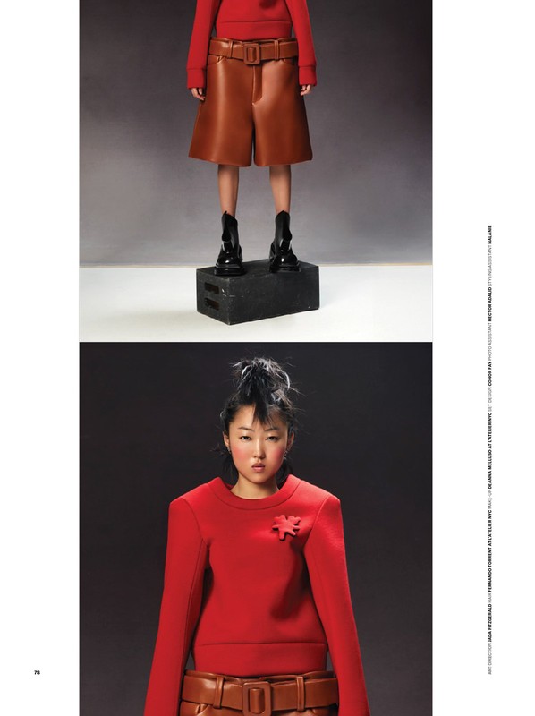 Fashion editorial shot of a woman in a red top and brown shorts, posing in a studio with a black cube platform.