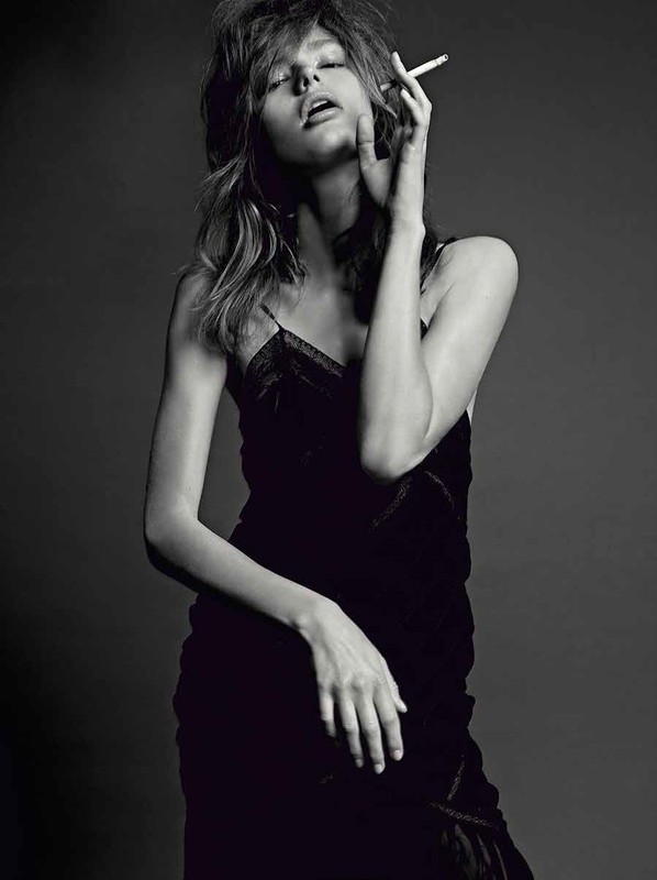 Black and white portrait of a young adult female in a velvet dress, smoking, with a neutral background, captured in a studio setting.
