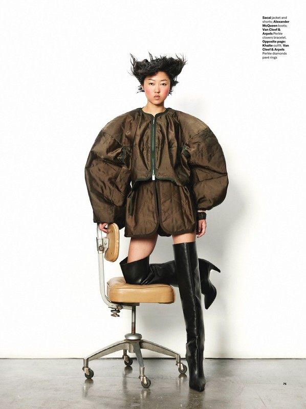 Editorial fashion shot of an Asian female model in a brown puffy jacket and shorts, posing with a tan rolling chair in a studio setting.