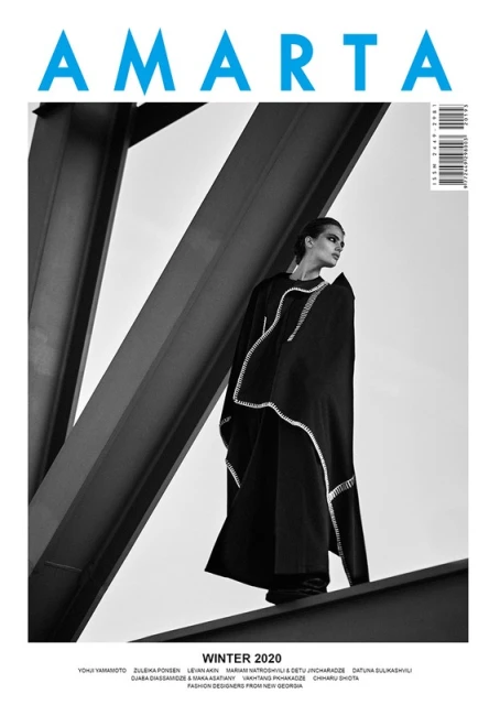 Fashion editorial cover of AMARTA magazine featuring a female model in a dramatic black dress, posing against a geometric steel structure.