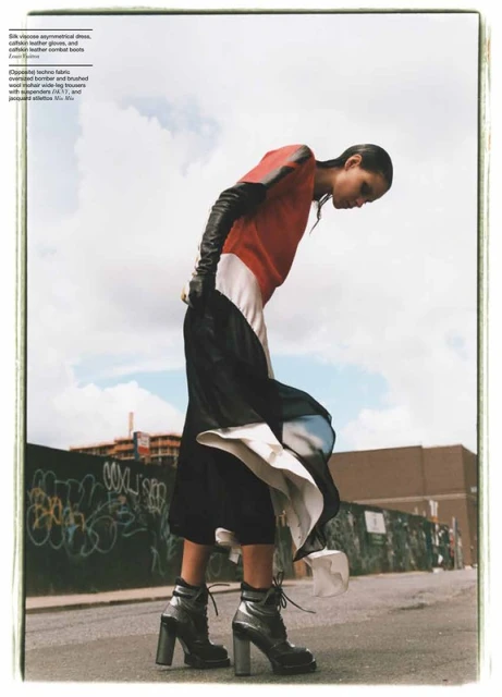 Fashion editorial shot of a woman outdoors wearing an asymmetrical dress, leather gloves, and combat boots against a graffiti wall.