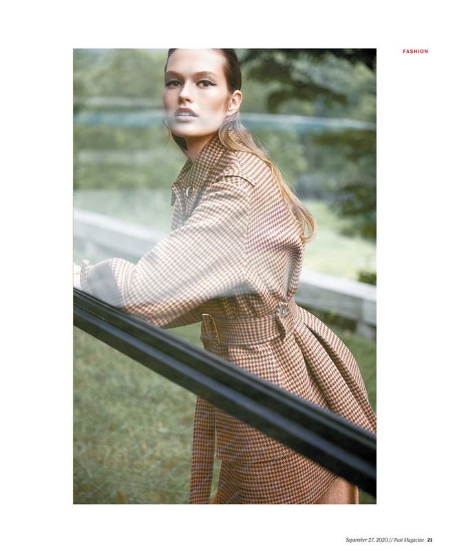 Model in brown houndstooth belted coat leaning against a railing in an outdoor park setting styled by Christine De Lassus