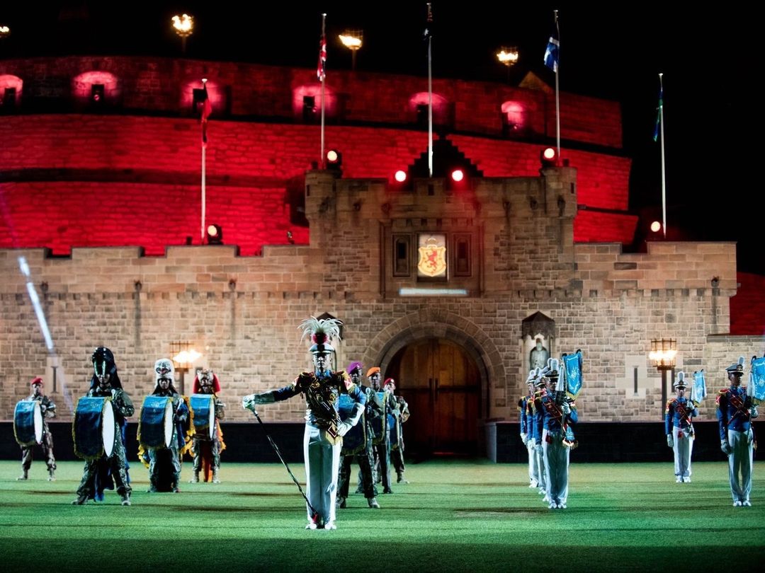 Marching band performs in front of stone castle at night with red stage lighting, creating a dramatic and captivating scene.