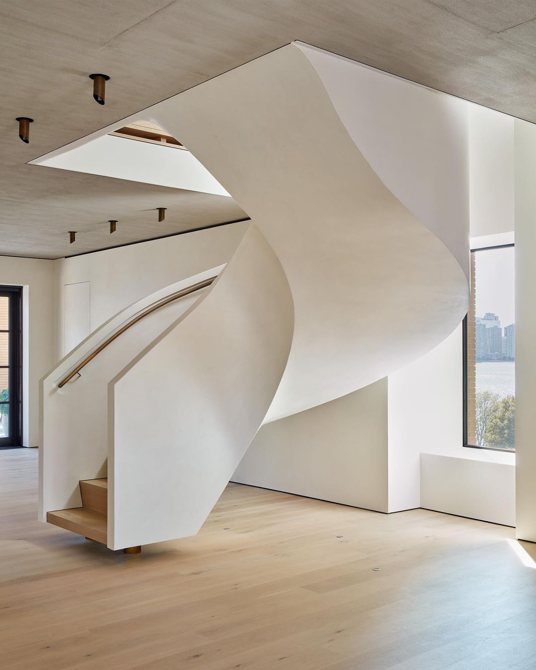 Interior view showcases a sculptural white staircase winding through a modern home with natural light and views of the outdoors.