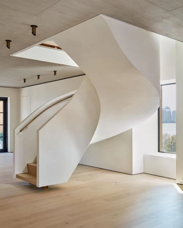Interior view showcases a sculptural white staircase winding through a modern home with natural light and views of the outdoors.