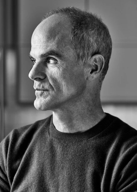 Black and white portrait of a mature adult man in a grey sweater looking off to the side, indoors with soft lighting. Studio portrait.