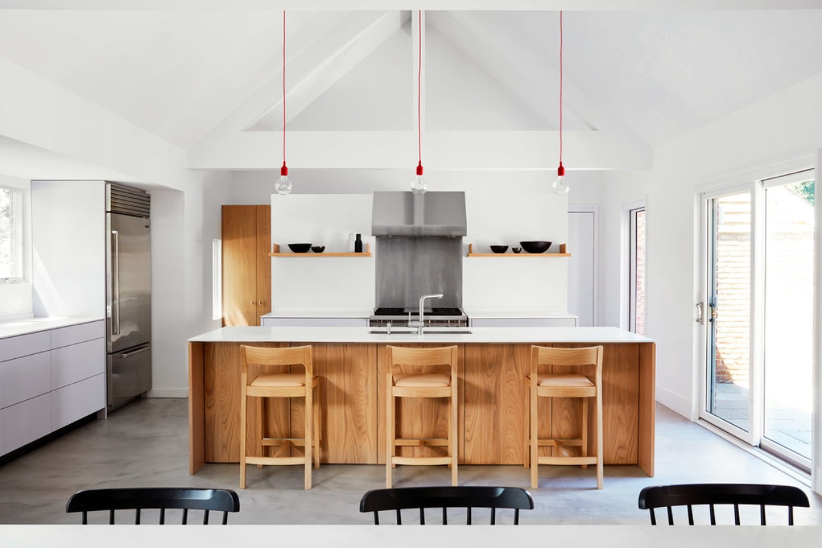 Bright, modern kitchen interior featuring a wood island with bar stools, stainless steel appliances, and minimalist design with red pendant lights.
