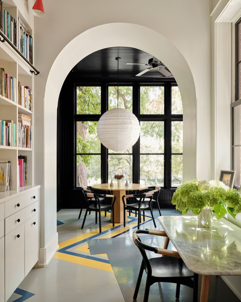 Bright, airy dining room with modern furniture: round table, black chairs, marble-top console, and patterned flooring, flooded with natural light.