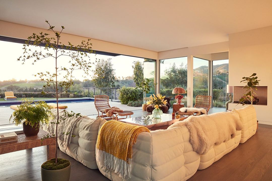 Bright and spacious living room with white sofa, rattan furniture, a glass coffee table, and a view of the outdoor pool and landscape.