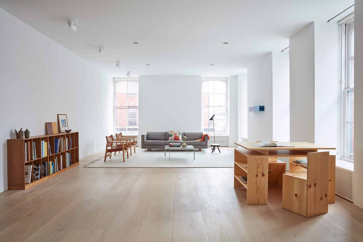 Modern interior featuring a gray sofa, wooden chairs and table, a bookshelf, and a bright, spacious room with large windows.
