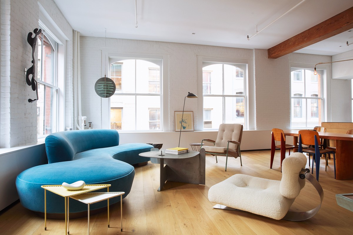 Bright and airy modern living room featuring a blue curved sofa, sculptural furniture, hardwood floors, and large windows.