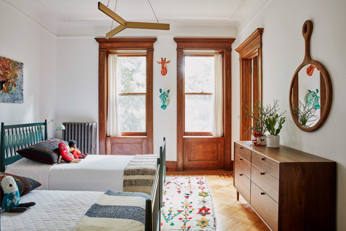 Bright children's bedroom with two beds, colorful rug, wooden dresser, animal wall art, and modern lighting fixture creating a playful interior.
