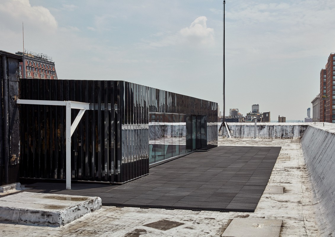 Rooftop view featuring a black modern structure with glass windows, surrounded by the cityscape and under a cloudy sky.