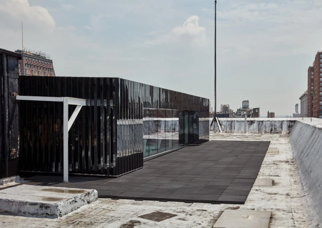 Rooftop view featuring a black modern structure with glass windows, surrounded by the cityscape and under a cloudy sky.