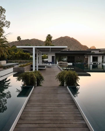 Exterior view of a modern house with a pool, deck, and mountain backdrop at sunset, showcasing architectural design and landscaping.