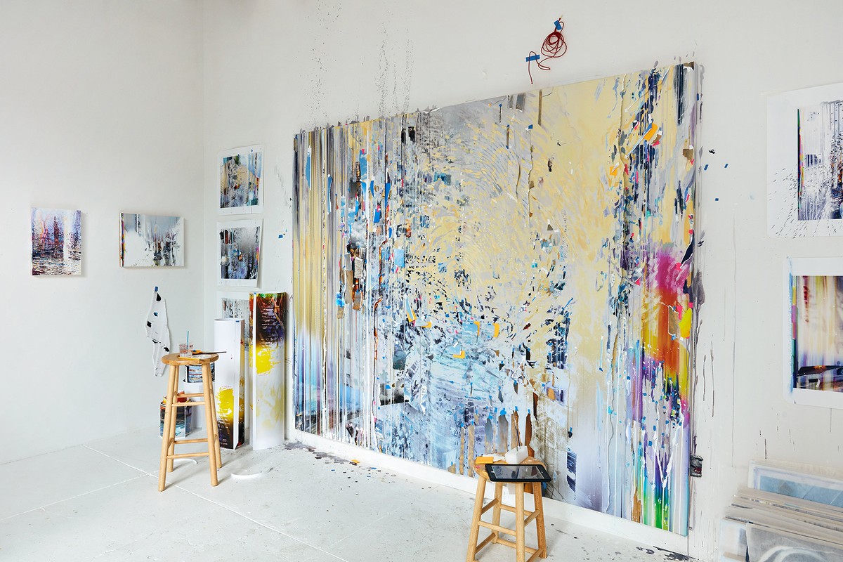 Large abstract painting displayed in a bright art studio, featuring a variety of colors and textures, with art supplies nearby.