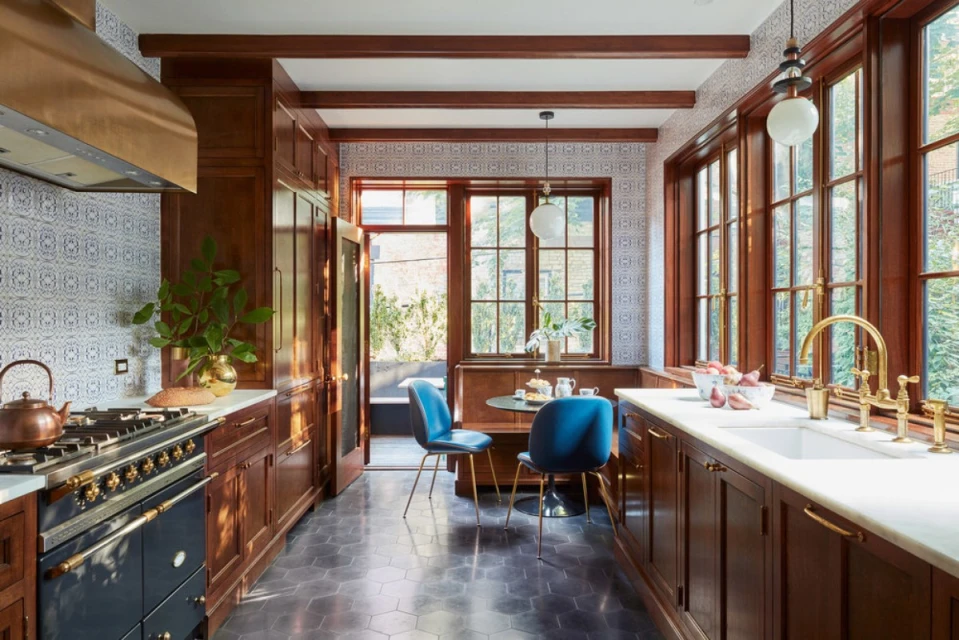 A home interior view of a kitchen with dark wood cabinets, white countertops, blue chairs around a table, and a range oven.