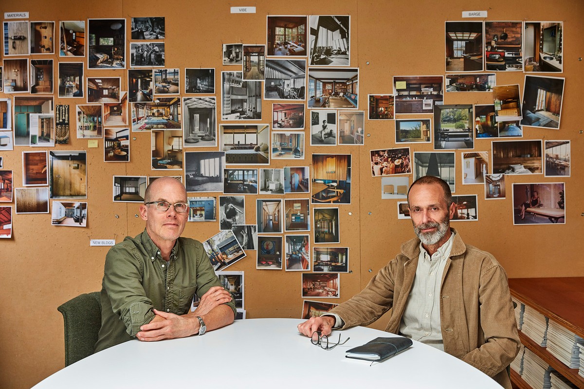 Two adult males in a meeting room with a corkboard featuring interior design photos, presenting an architectural concept in a modern style.