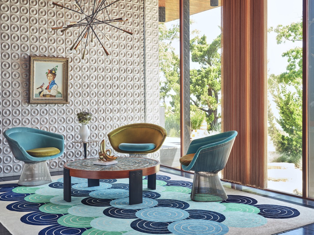 Living room interior showcases mid-century modern design with armchairs, patterned carpet, and art, illuminated by natural light.