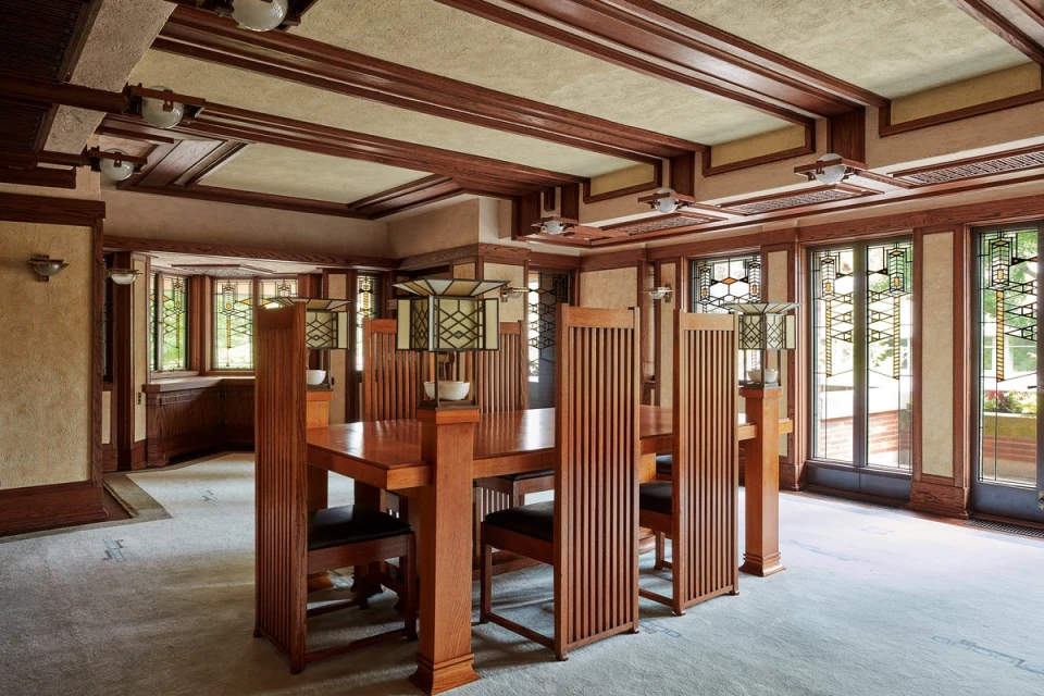 Warm-toned interior with wood dining table and chairs. Stained-glass windows add color to the light-filled dining room with unique light fixtures.