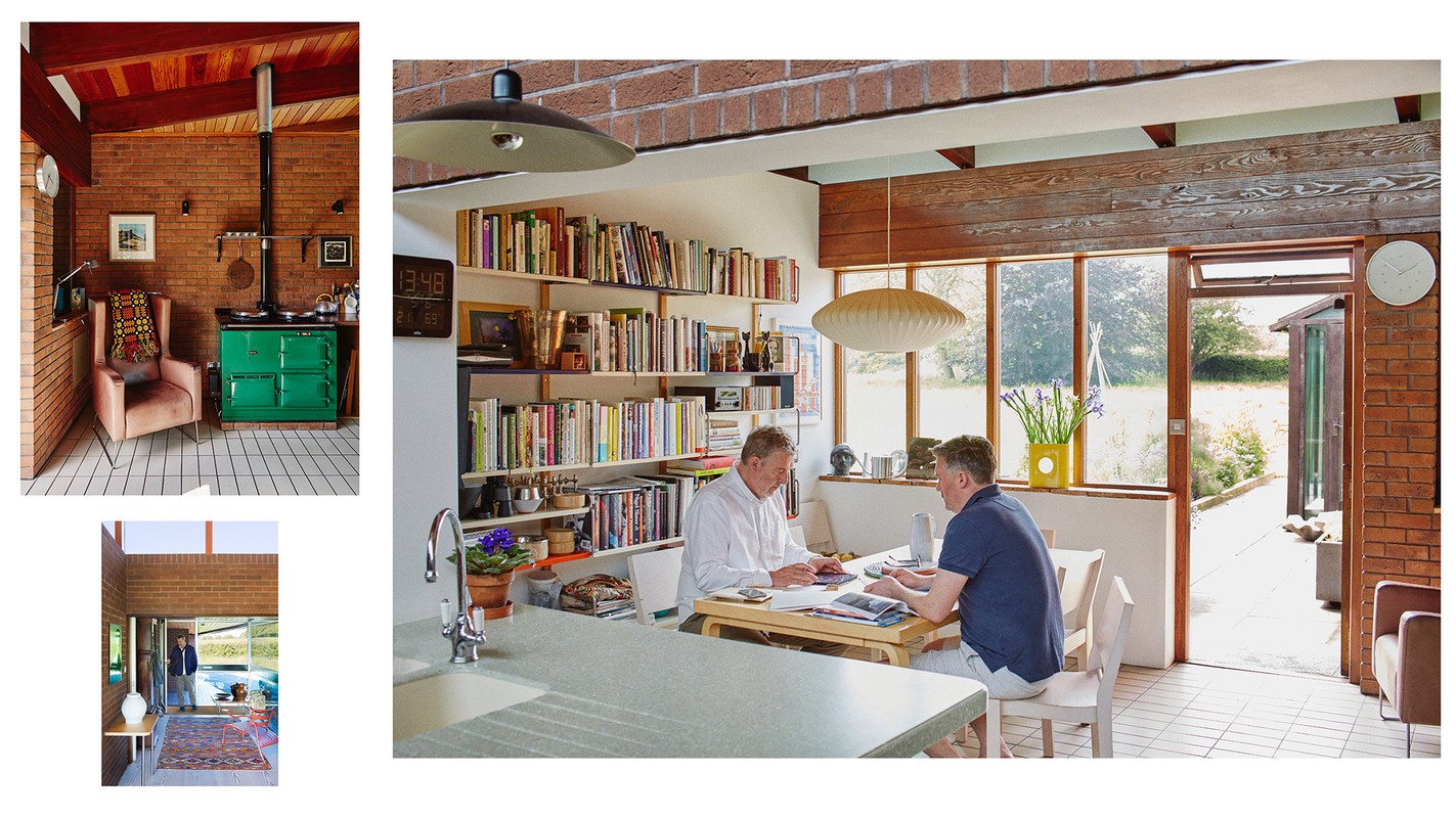 Two men working at a table in a modern house interior featuring brick walls, bookshelves, large windows, and natural light.