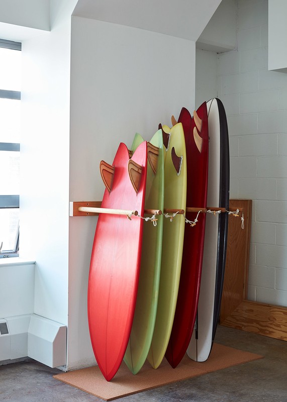 Colorful surfboards are neatly stacked in a storage rack against a white wall in a well-lit indoor area, creating a vibrant display.
