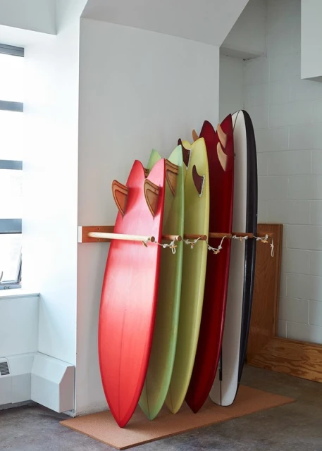 Colorful surfboards are neatly stacked in a storage rack against a white wall in a well-lit indoor area, creating a vibrant display.